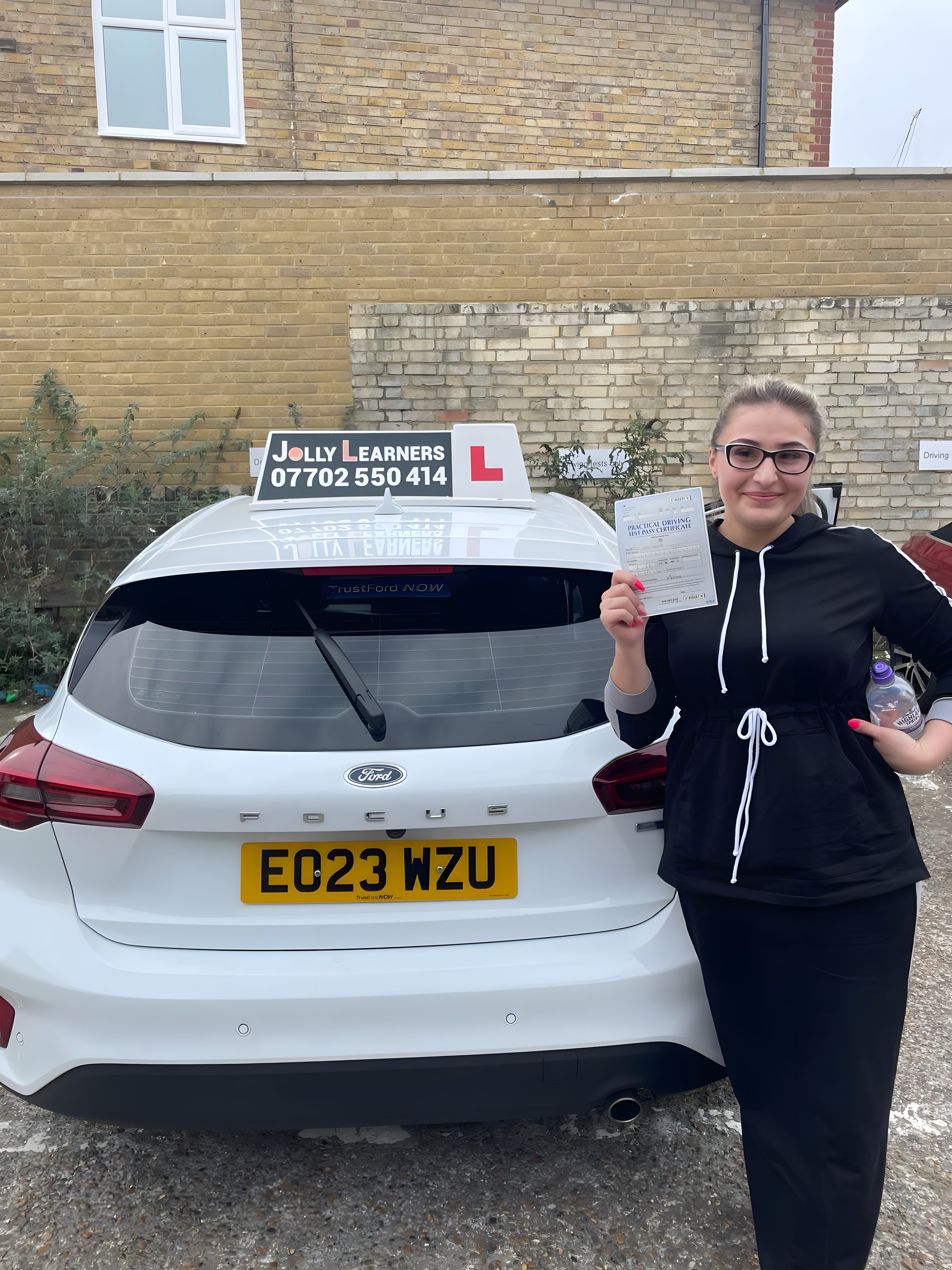 A learner holding a practical driving test pass certificate beside the branded Jolly Learners tuition car